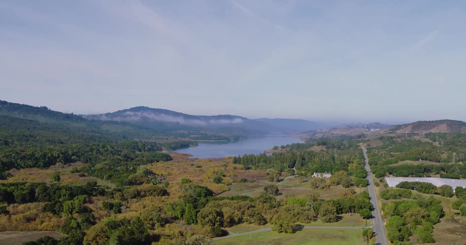 Aerial panoramic view of green rural farmland surrounding a lake in a mountain valley during the day