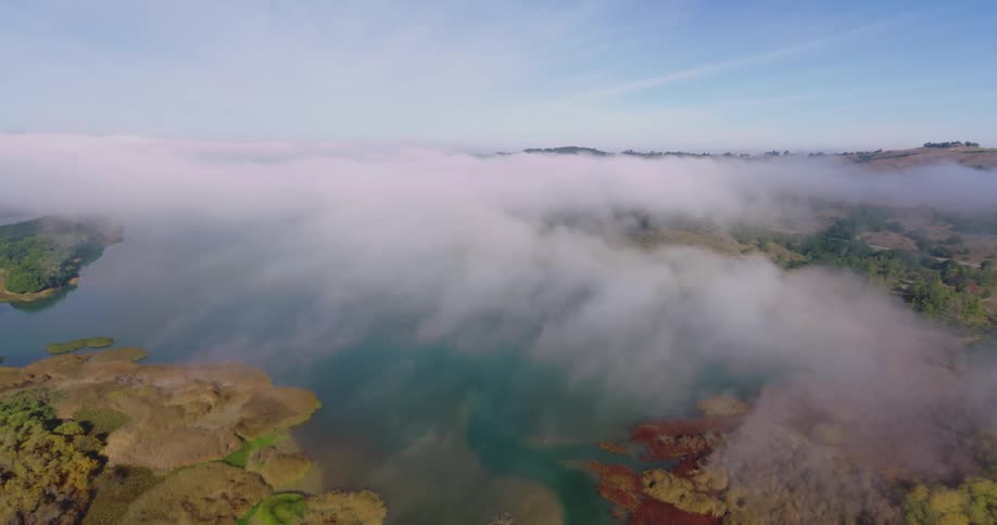 A thin layer of clouds hangs low in the sky above forests and rivers