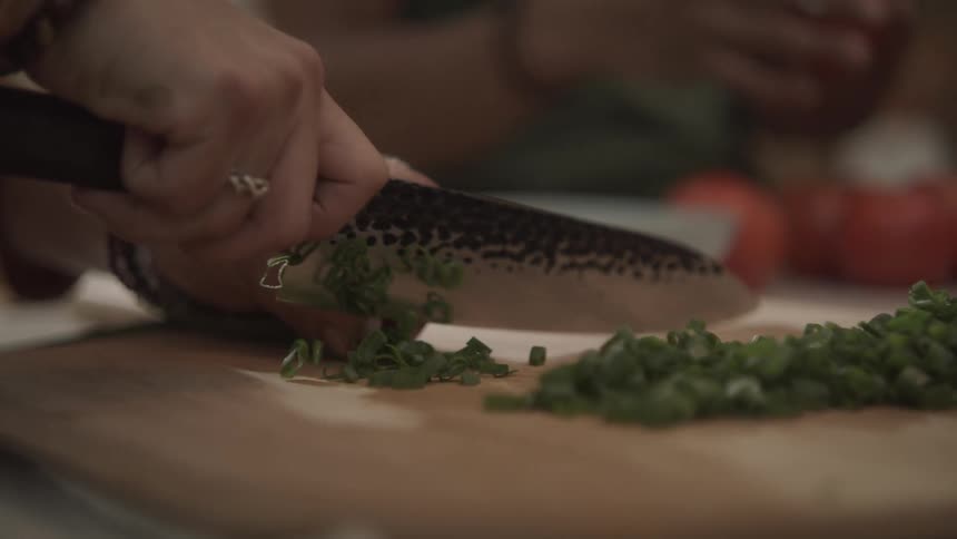 A human hand using a large knife to cut green vegetables that are on top of a cutting board