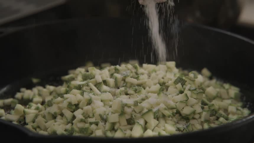 A person pours salt on the food in the pan