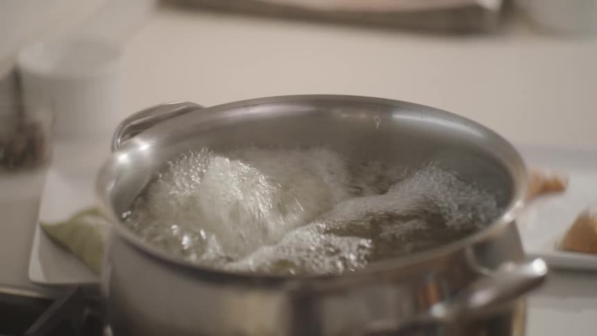 Person works in kitchen as liquid boils in metal pot on stovetop