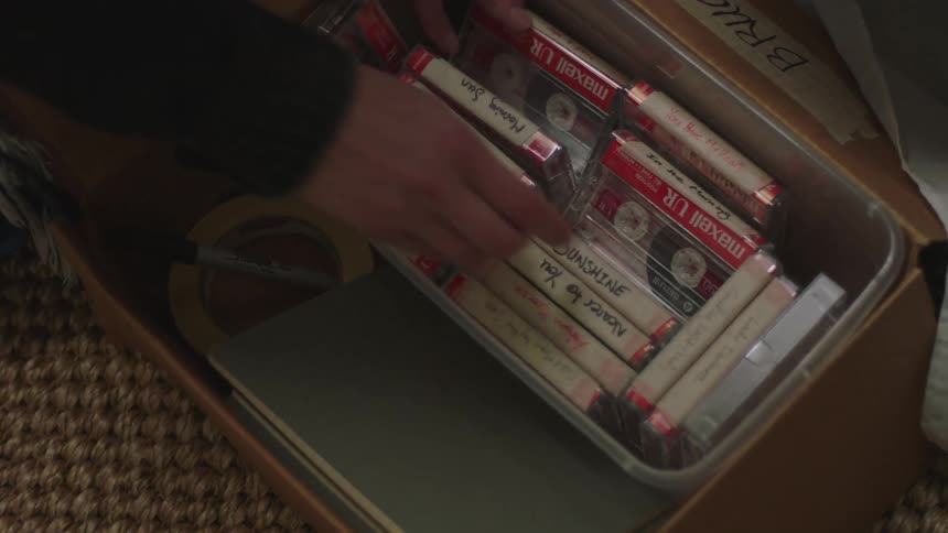 Lady brings out a carton full of cassette tapes from under the bed and took one out