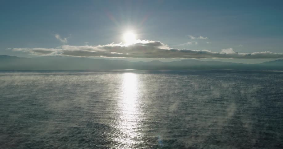 The sun shines brightly above the clouds and reflects on the water below