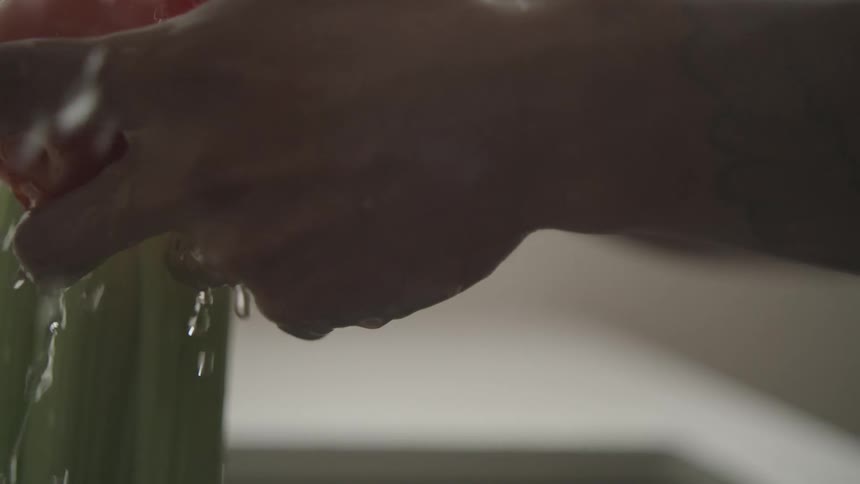 A person washing vegetables in the sink at home