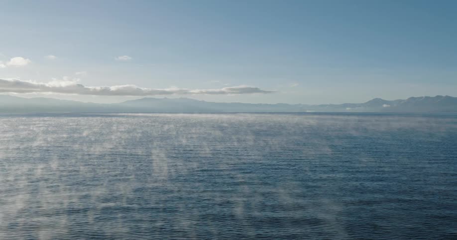 Thin fog clouds on top of a blue sea with a blue sky on a bright day