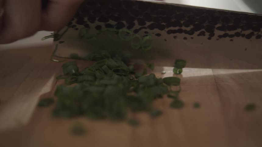 A human hand using a large knife to cut green vegetables