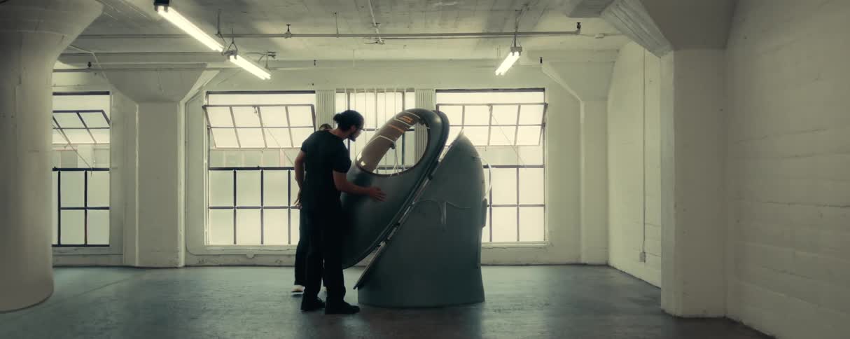 Coworkers wearing scrubs examine large open medical pod in empty room with open windows