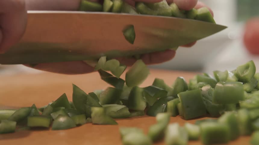 A person scoops up the chopped peppers with a knife and puts it in a bowl