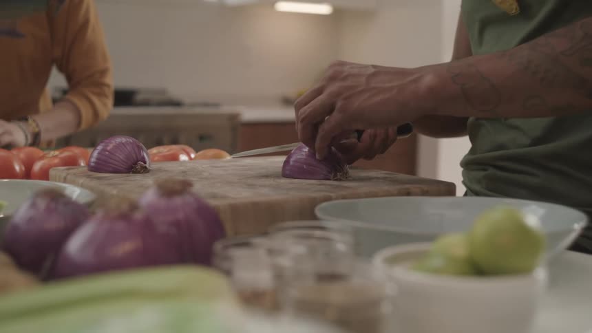 Closeup of a person chopping a red onion on a cutting board in the kitchen