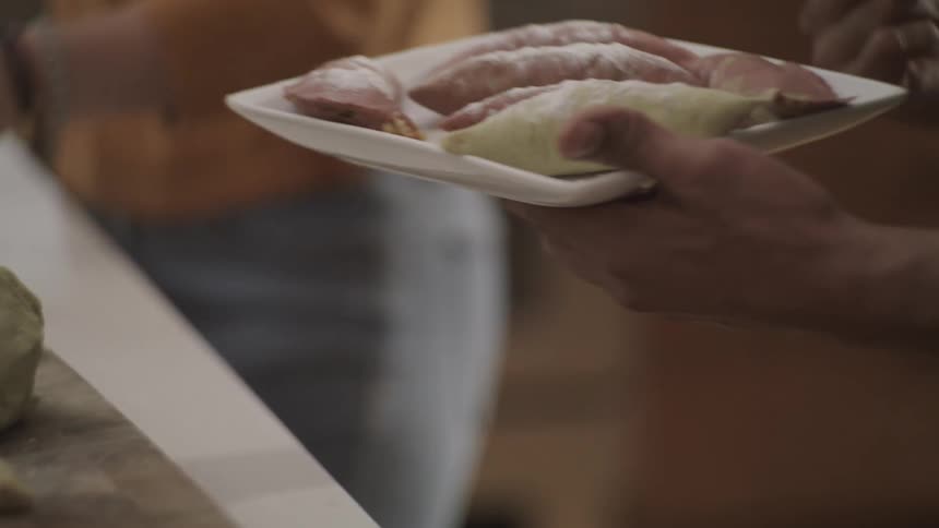 Woman hands man a plate of prepared meat near a kitchen counter full of food
