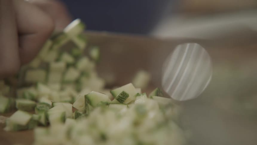 An adult is chopping vegetables with a large chopping knife