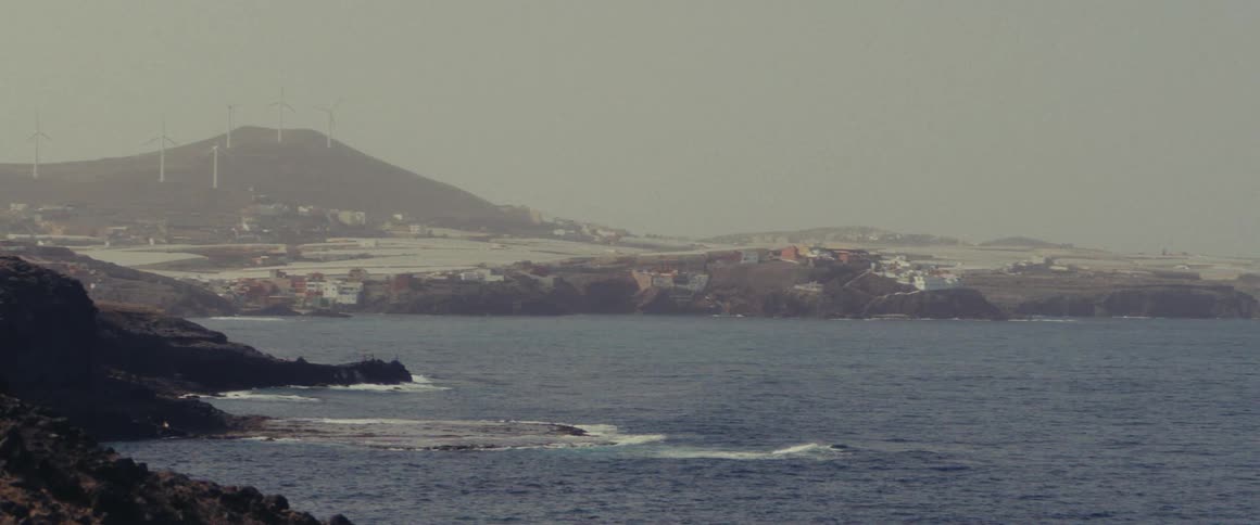 Fog obscures wind turbines on mountain overlooking coastal town