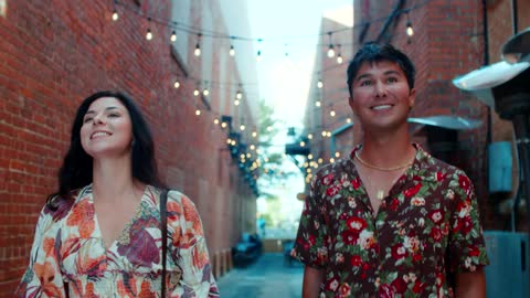 A man and a woman are talking and walking on a path between brick buildings