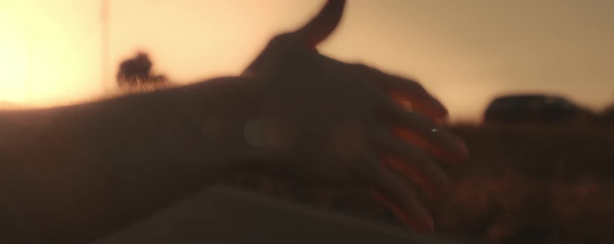 View of the arm and hands of a person sticking out of a car enjoying the natural breeze under a reddish dawn sky