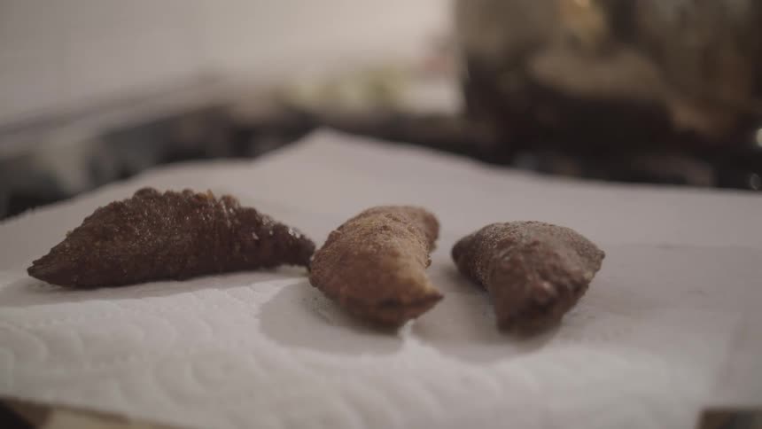 Someone uses tongs to place fritters on paper towels