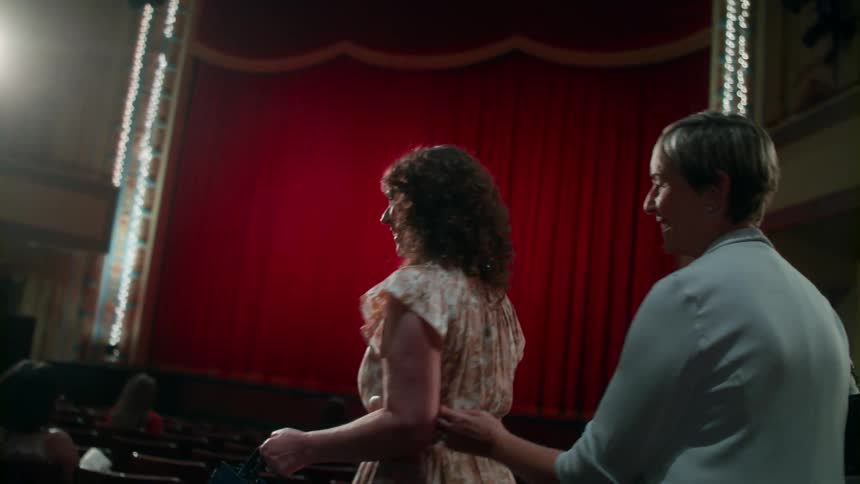 Women arriving in theater walk down row of seats before the show starts