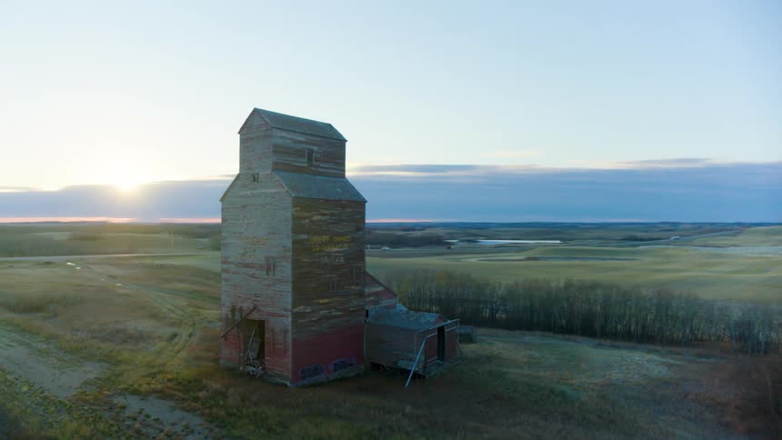 Old mill with peeling red paint sits between railroad tracks and a field