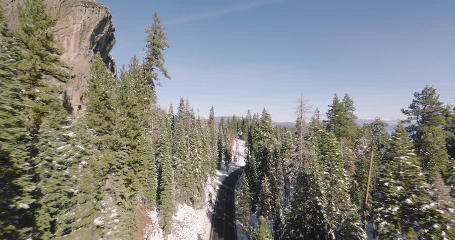 Aerial over stream through a snowy forest emptying into a lake during the day