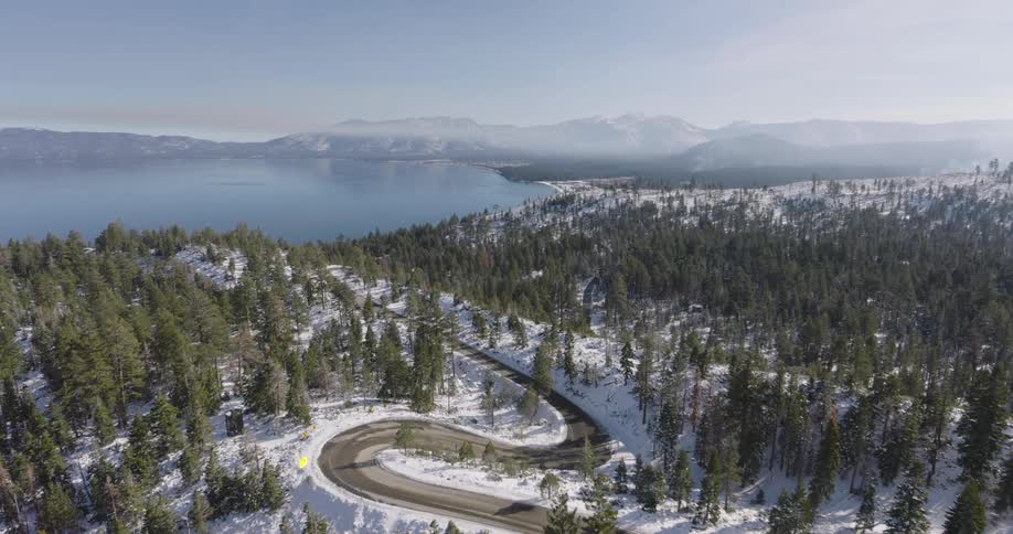 Cars travel on a winding road across the top of a snow covered forested mountain along the coast