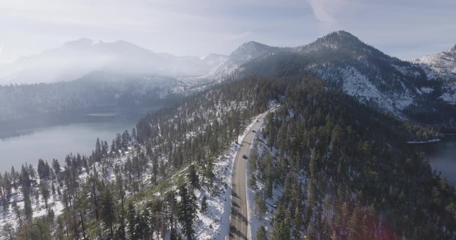 Aerial view of a mountain ridge road and mountain peaks covered in fog in the background on a sunny day