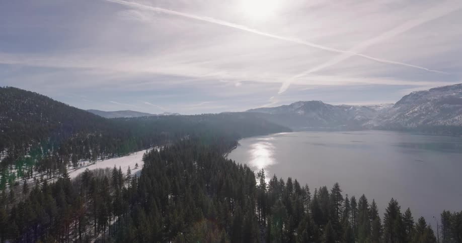 Aerial panorama of a mountain range with snow and coniferous trees around a lake