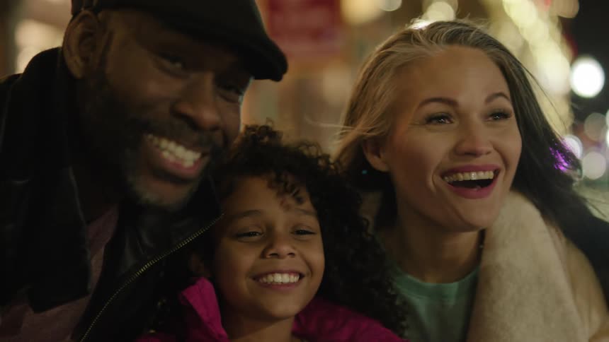 A woman and an adult man with a child in the middle are happy and smiling posing for something