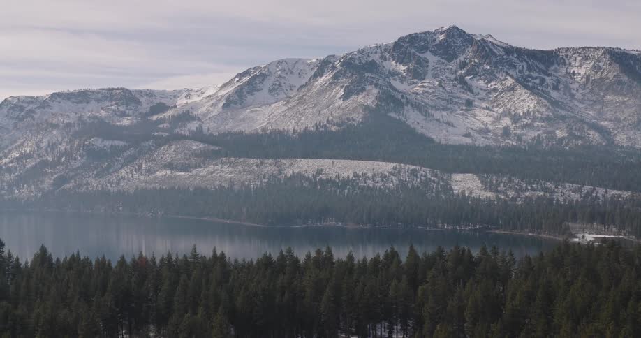 Aerial panorama of a mountain range covered in snow and conifers with a central lake