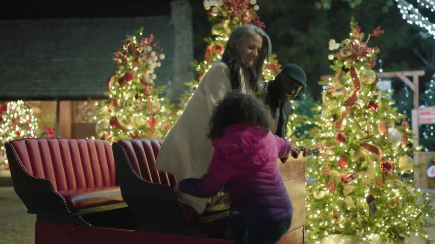 Family board a decorative sled next to christmas trees