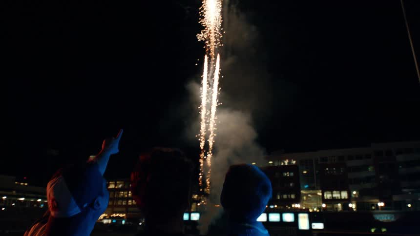 One of two men hold boy as they watch fireworks display at night