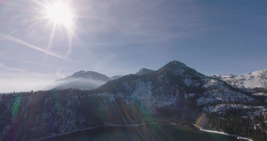 Mountians and a lake in the winter covered by the glare from the sun in a blue sky above them
