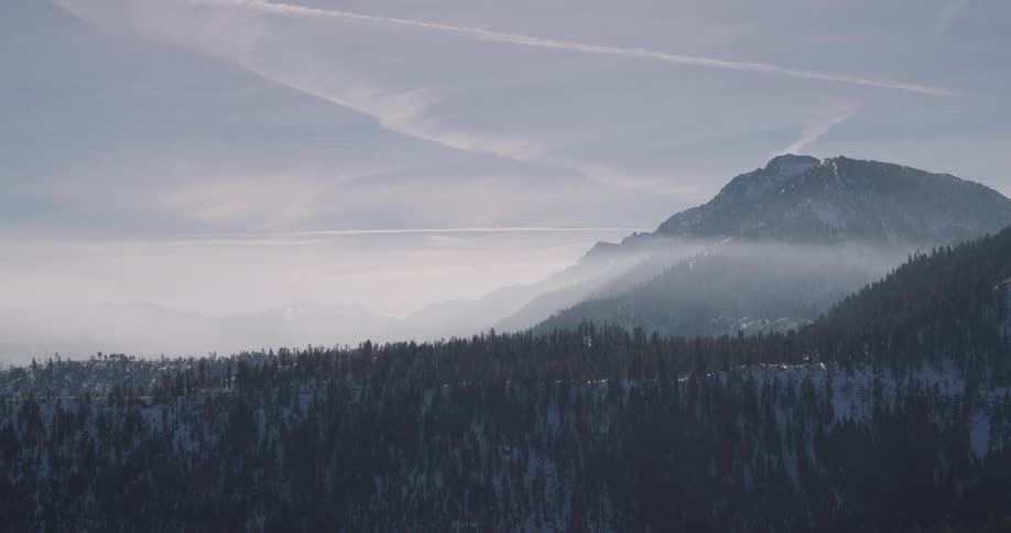 Panorama of a mountain range with coniferous trees and snow on a day with a cloudy sky