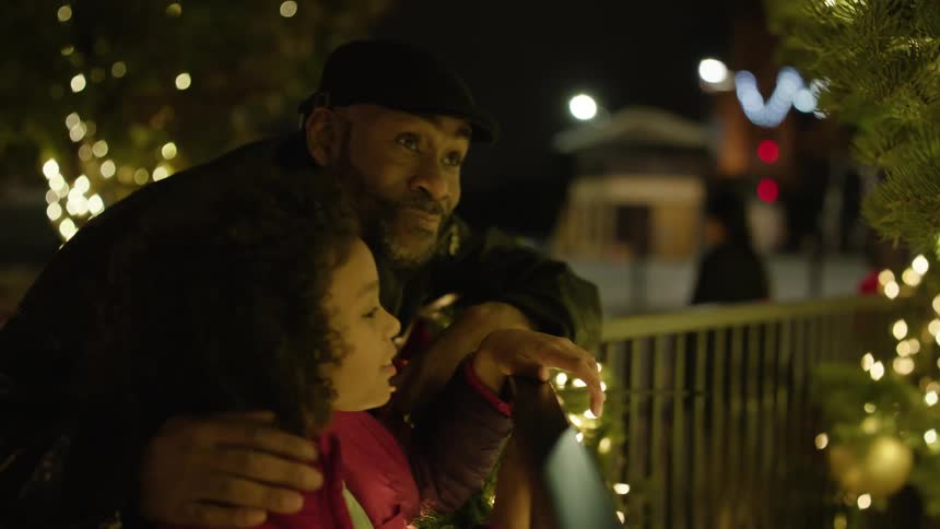 Father and daughter talking and smiling while touching a christmas tree outdoor at night
