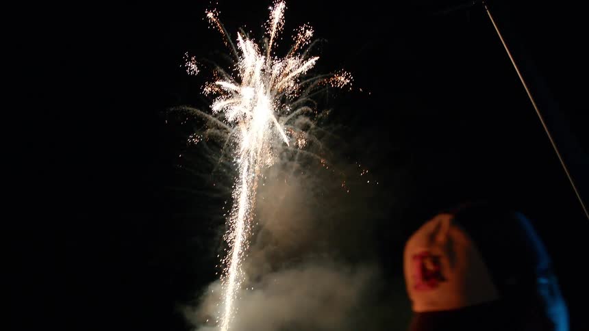People stand watching fireworks shoot into the night sky over midrise buildings