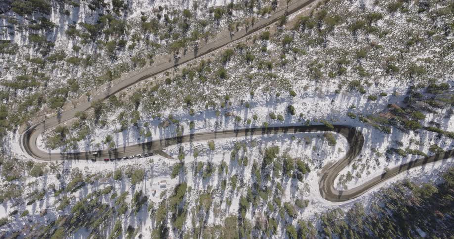 A truck travels on a winding road through snow covered forested land