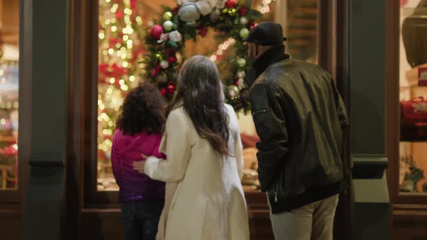 Parents with their daughter looking at an outdoor shop window with a christmas wreath