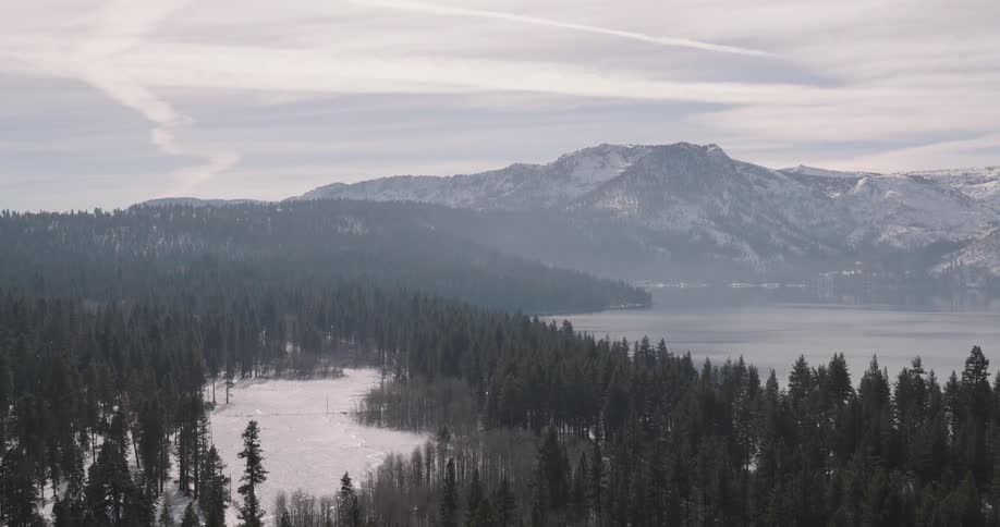 Aerial of a frozen lake with snowcovered forest during dusk