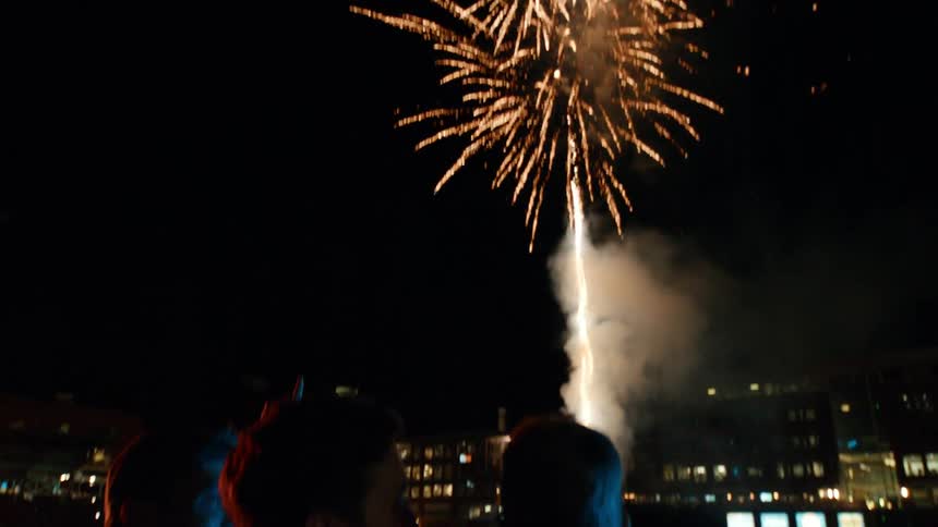 People watching from beside a green lawn with fireworks shooting fountain style into the night sky creating a shower of gold light trails expanding in all directions
