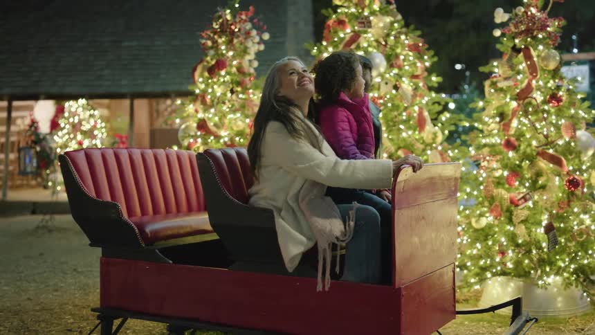 Family having fun over a sled next to christmas trees