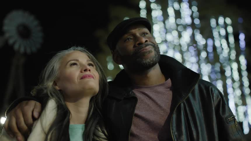 Man and woman hugging in an outdoor setting with lights at night