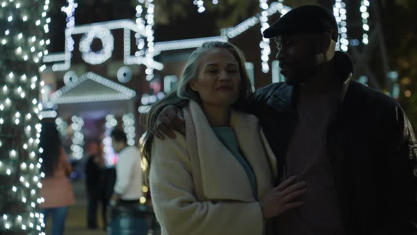 Couple enjoys a romantic moment in the white christmas lights outside a large home