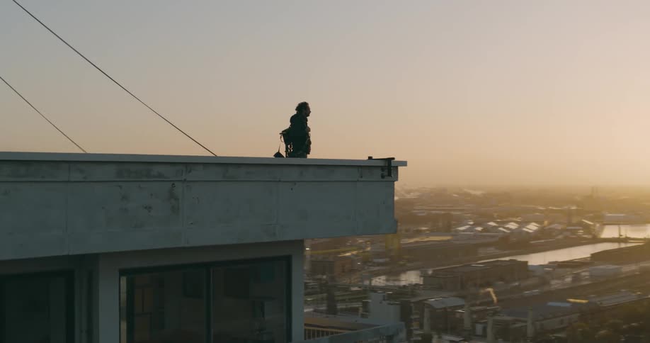 The silhouette of a person on top of a building looking at the horizon and the sun shining in the sky
