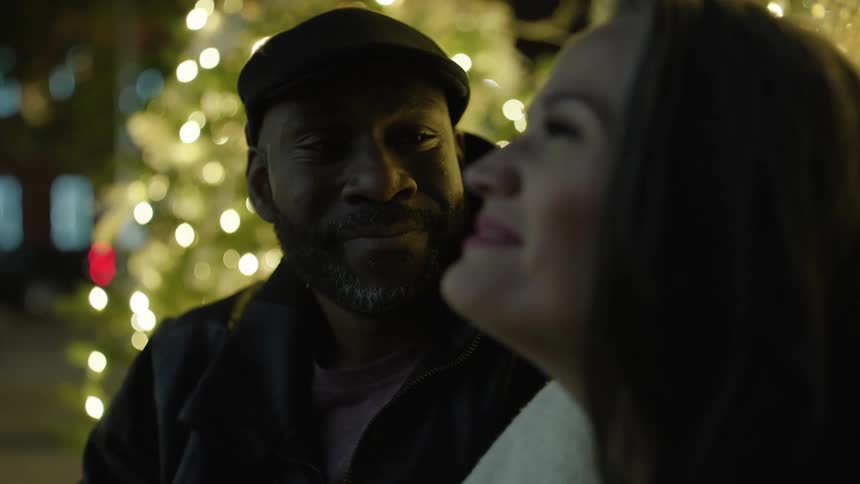 Man looking romantically at his woman beside trees adorned with christmas lights at night