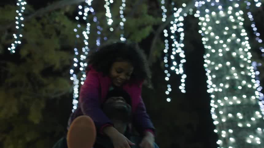 Happy girl riding on her father shoulders looking at christmas decorations