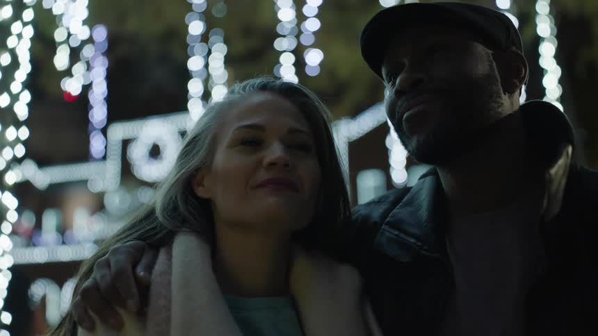 Happy couple surrounded by christmas lights look lovingly at each other