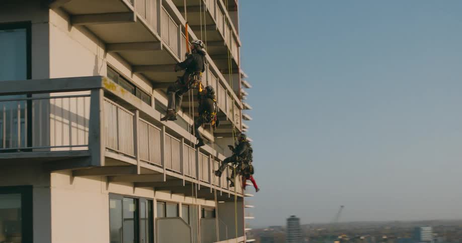 Men are hanging off the building terrace doing repairs