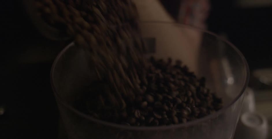 Coffee beans are poured from a clear bucket into a machine