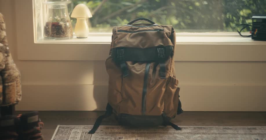 Hiker wearing socks picks up backpack resting on floor near window