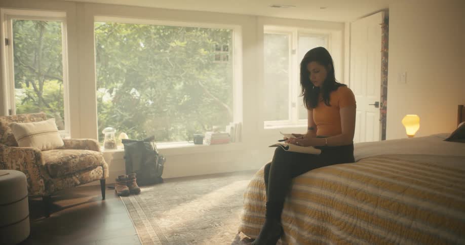 Woman writing in bed stands up to pick up her backpack and boots