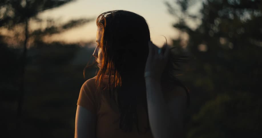 Woman wearing an orange t shirt looks over her shoulders in the forest