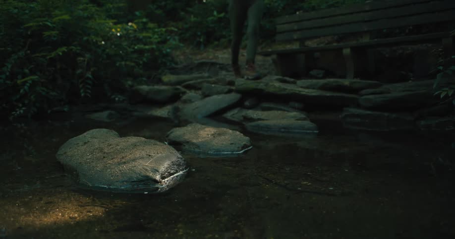 A person walking in the forest jumps over rocks on a river
